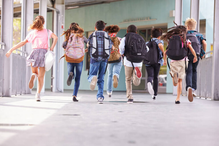 students in backpacks running toward their school