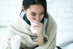 sick person wiping their nose while wrapped in a blanket